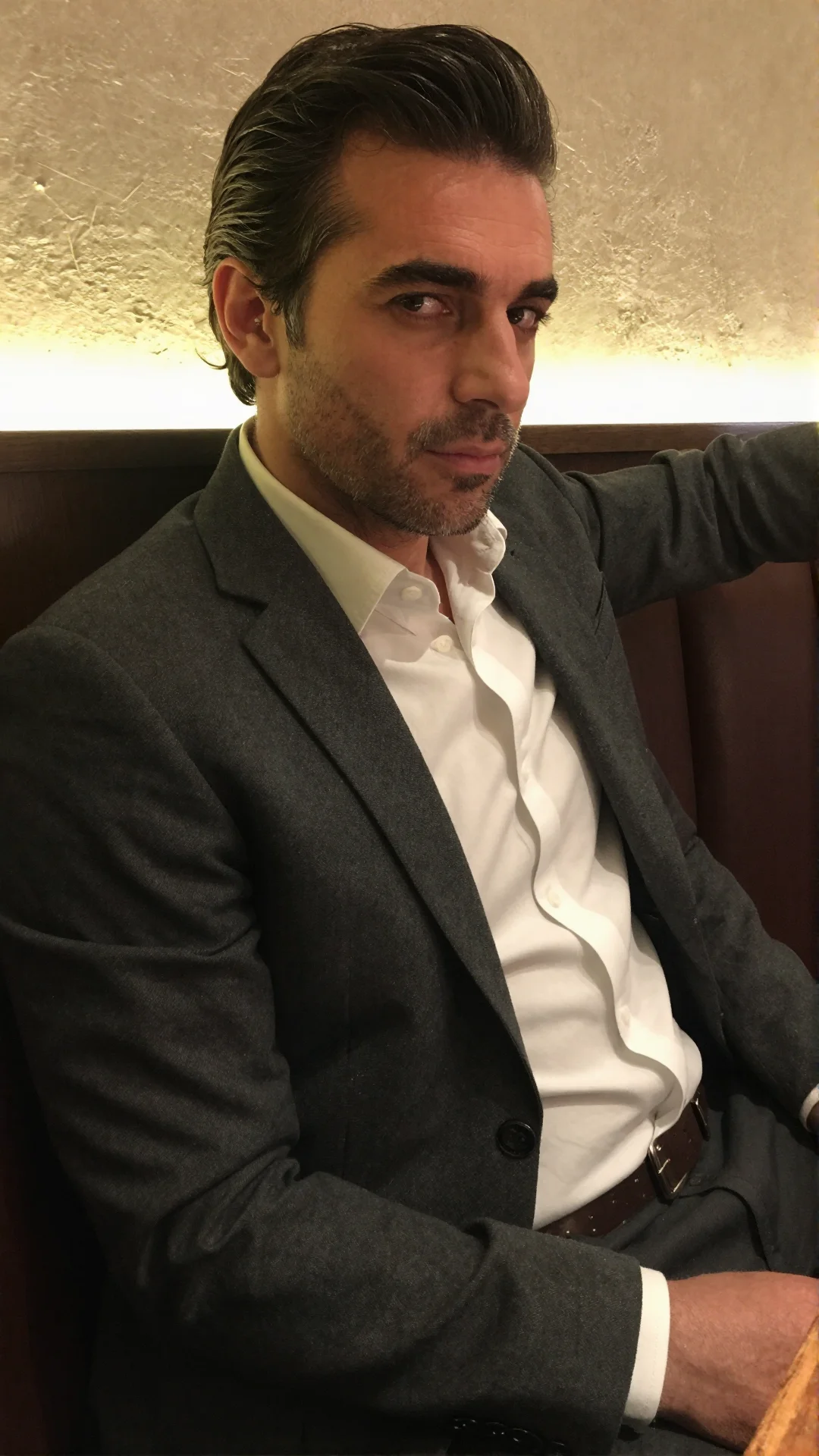 Serious Italian man in an open-collar shirt and charcoal jacket in a restaurant booth