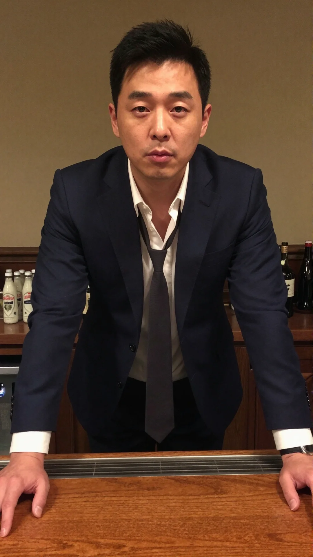 Serious Korean man in a loosened suit and open collar at a hotel bar