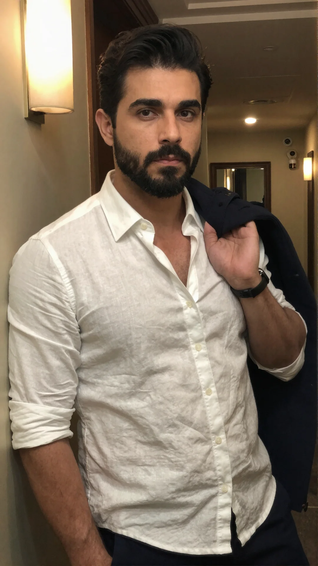 Serious Peruvian man in an open linen shirt with a coat over his arm in a hotel hallway