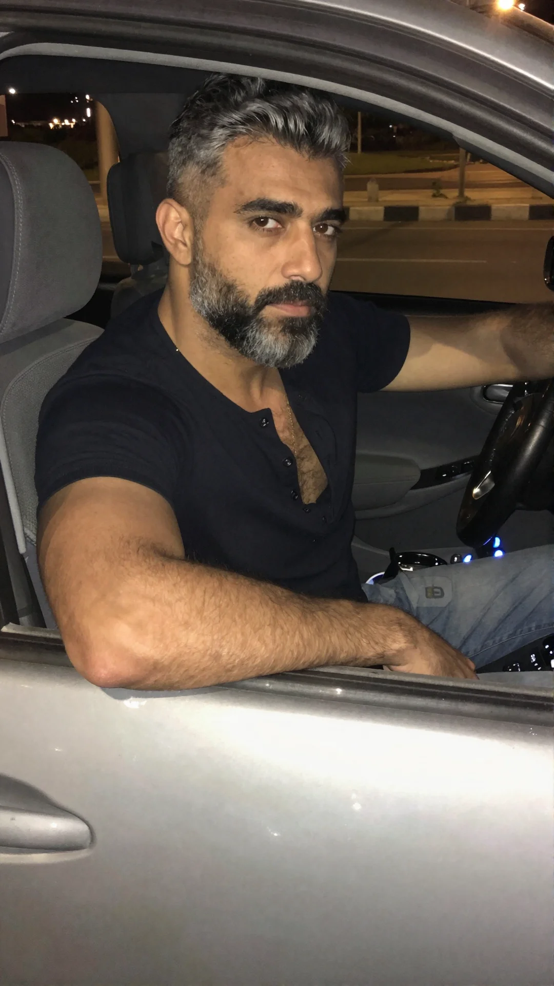 Serious Egyptian man in an open shirt in the driver seat of a car at night